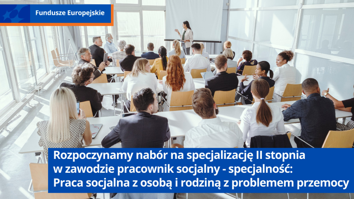 Pomieszczenie biurowe. Kobiety i mężczyźni w różnym wieku siedzą przy stolikach. Przed nimi kobieta stoi przy rozwijanej tablicy